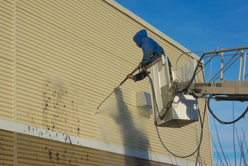 Man on a crane pressure washing a wall