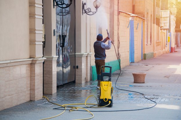 man pressure washing a lamp outside of a building