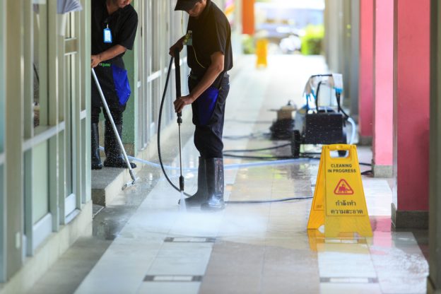 Workers pressure washing a floor and a wet floor sign