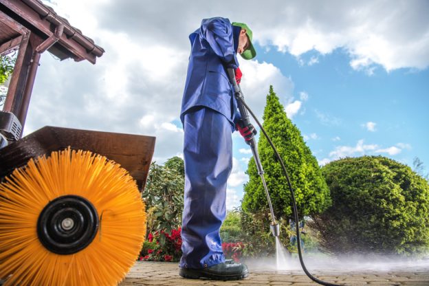 Man in a hazmat suit using a pressure washer in the summer