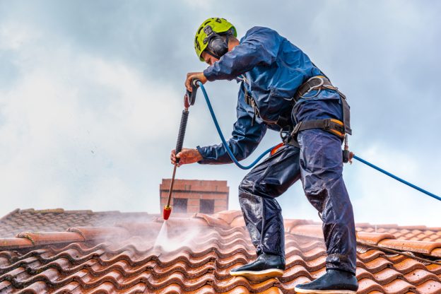 Man using a pressure washer on a roof